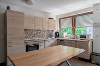Koch- / Wohnbereich der WG Ansbach: Zu sehen ist eine moderne L-Küche in Holzoptik, direkt an einem breiten Fenster gelegen. Im Vordergrund ein großer Esstisch.
