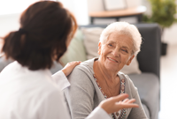 Pflegefachkraft und lächelnde Seniorin im freundlichen Gespräch. Pflegefachkraft in Rückenansicht.